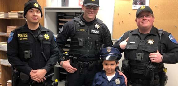 Three officers of Tulalip Tribal Police with young child in uniform, experience chief for a day mobile image.